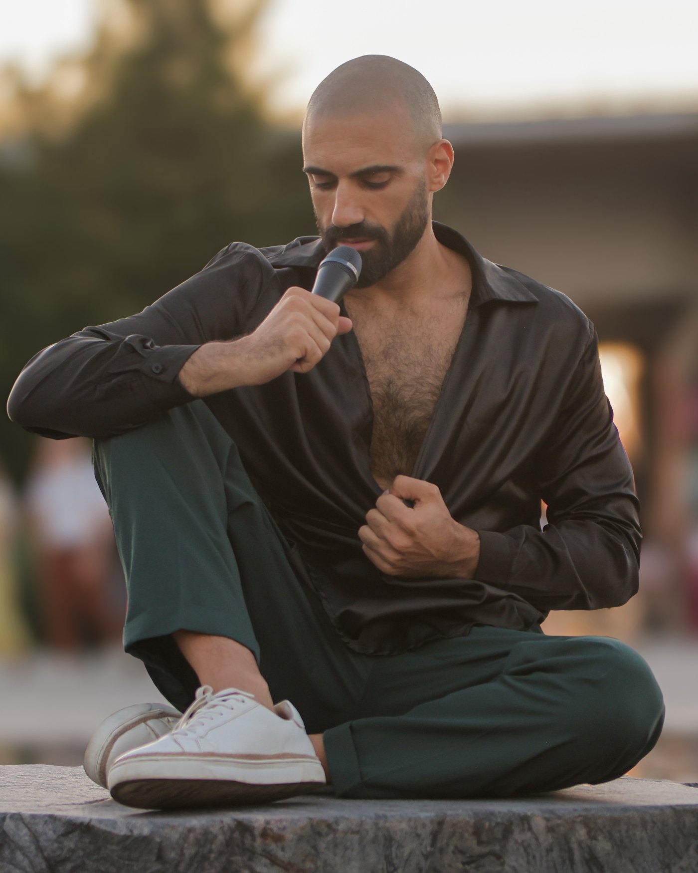 Sami Harb seated outdoors at golden hour, singing softly into a microphone